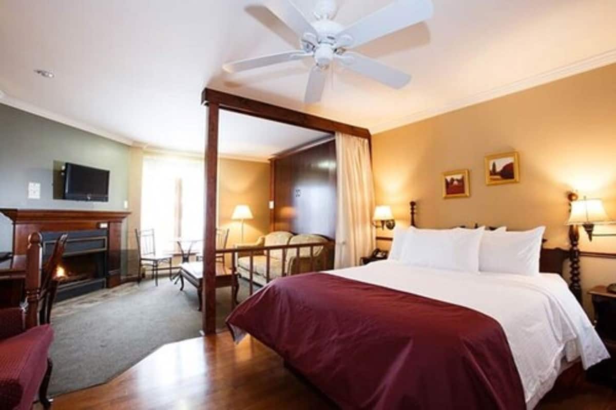 A hotel room with a four-poster bed, a fireplace, a television, and a dining area with a table and chairs.