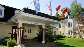 Een hotel receptie met een overdekte ingang, vlaggen en een verzorgd gazon.