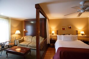 A hotel room with a bed, a desk, a chair, a sofa, a ceiling fan, and two bedside lamps. - Relais St-Denis (Saint-Sauveur)