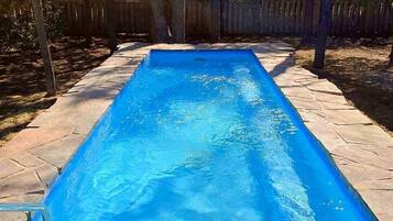 Una piscina rectangular con agua azul cristalina, rodeada por un solárium de piedra y una valla de madera.