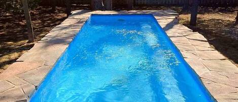 Une piscine rectangulaire à l’eau d’un bleu limpide, entourée d’une terrasse en pierre et d’une clôture en bois.