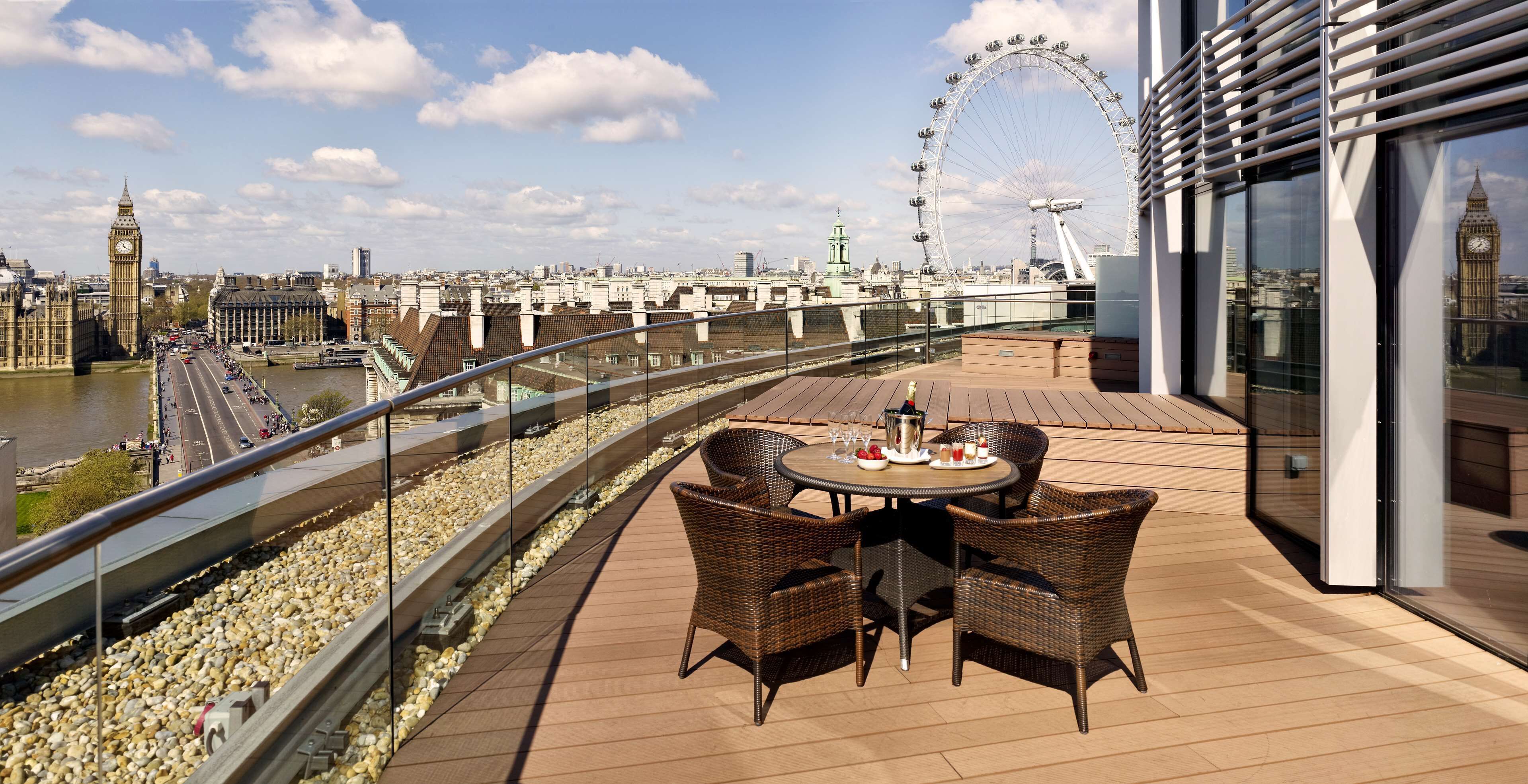 Un balcón con mobiliario de mimbre, una mesa con bebidas y vistas al río y a los monumentos de Londres.