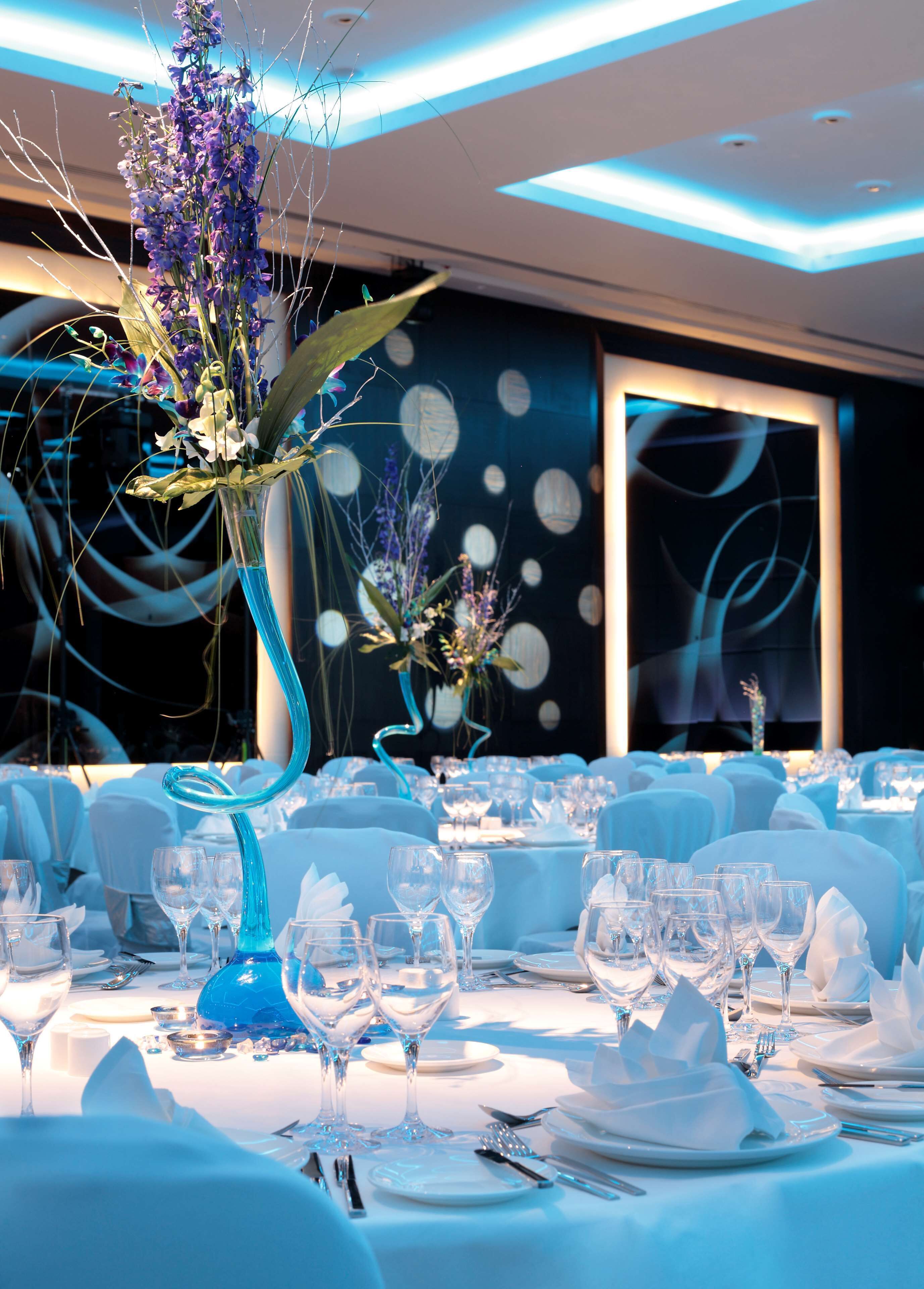 A banquet hall with tables set for a formal event, featuring blue tablecloths, white napkins, and clear glassware.