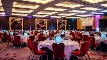 Un salón de banquetes con mesas redondas, sillas rojas y una gran pantalla que muestra 'Park Plaza Westminster Bridge London'.
