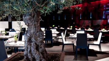 A restaurant with a large tree centerpiece, tables, chairs, and a modern interior design.