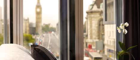 A hotel room with a view of a cityscape, including a clock tower, through large windows.