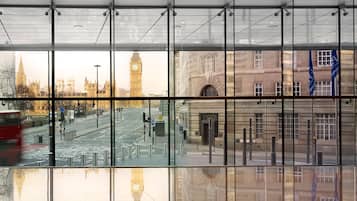 A modern building with large glass windows reflecting a cityscape, including a clock tower and historic buildings.
