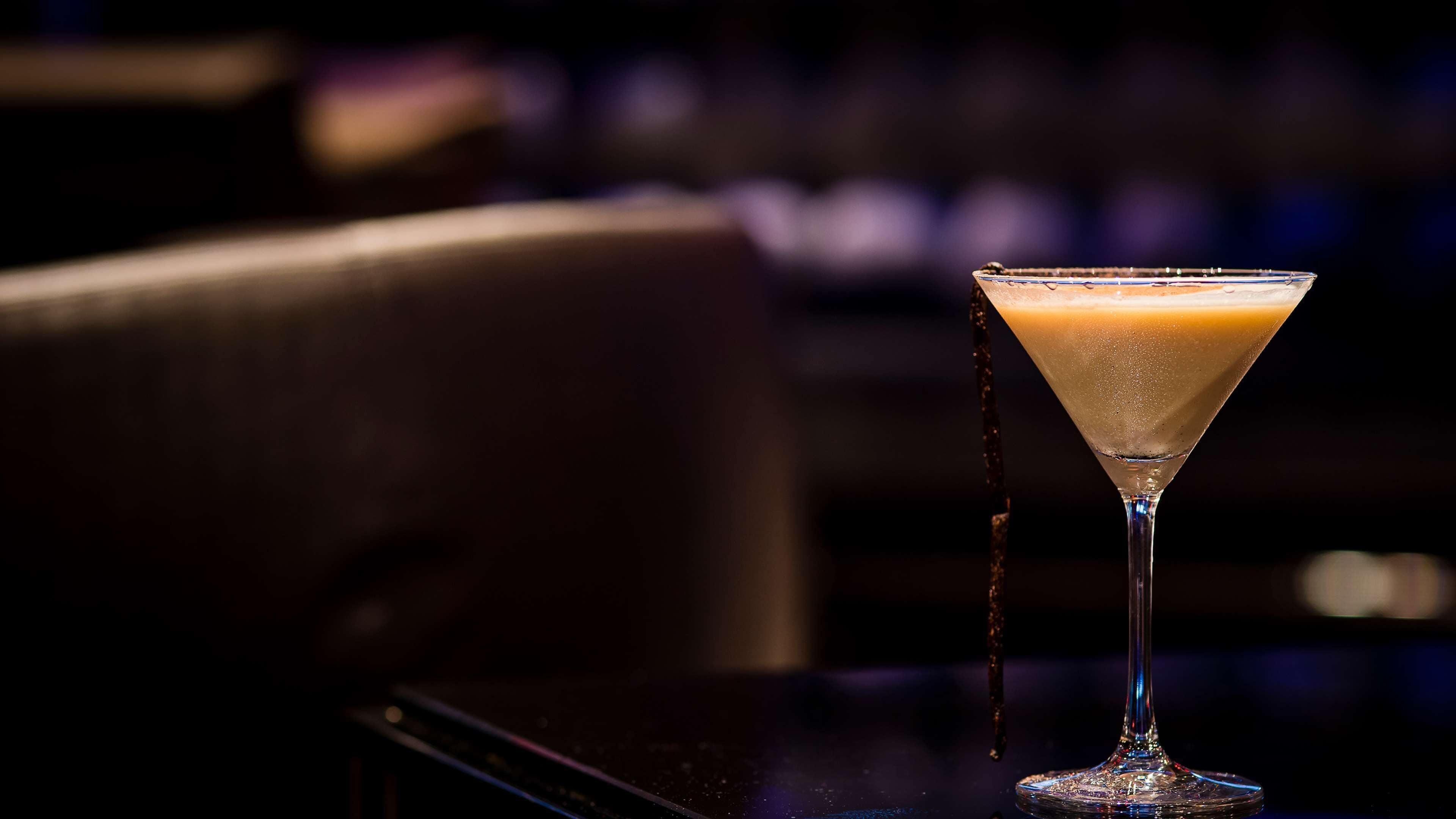 A martini glass with a frothy drink on a bar.