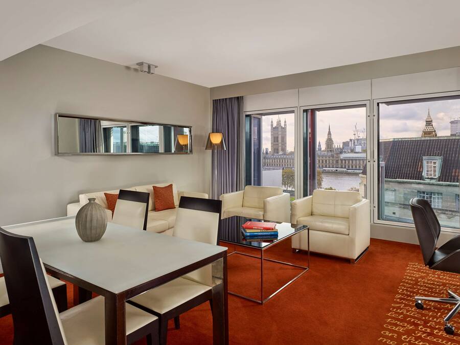 Una habitación de hotel moderna con zona de comedor, un sofá, una mesita de centro y vistas a la ciudad.