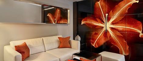 A modern living room with a white sofa, a glass coffee table, and a large floral artwork on the wall.
