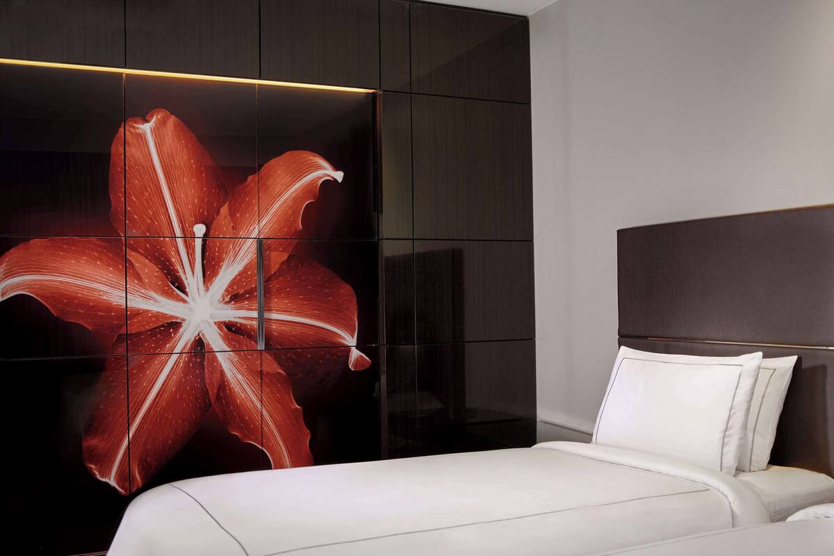 Una habitación de hotel moderna con una cama grande, un armario oscuro y una obra de arte floral de gran tamaño en la pared.