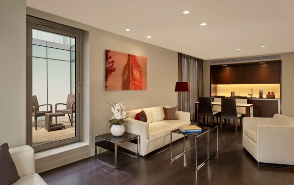 A modern living room with a sofa, coffee table, and chairs, a dining area with a table and chairs, and a kitchen with a counter and appliances.