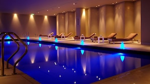Une piscine avec des lumières bleues, des chaises longues et un sol carrelé.