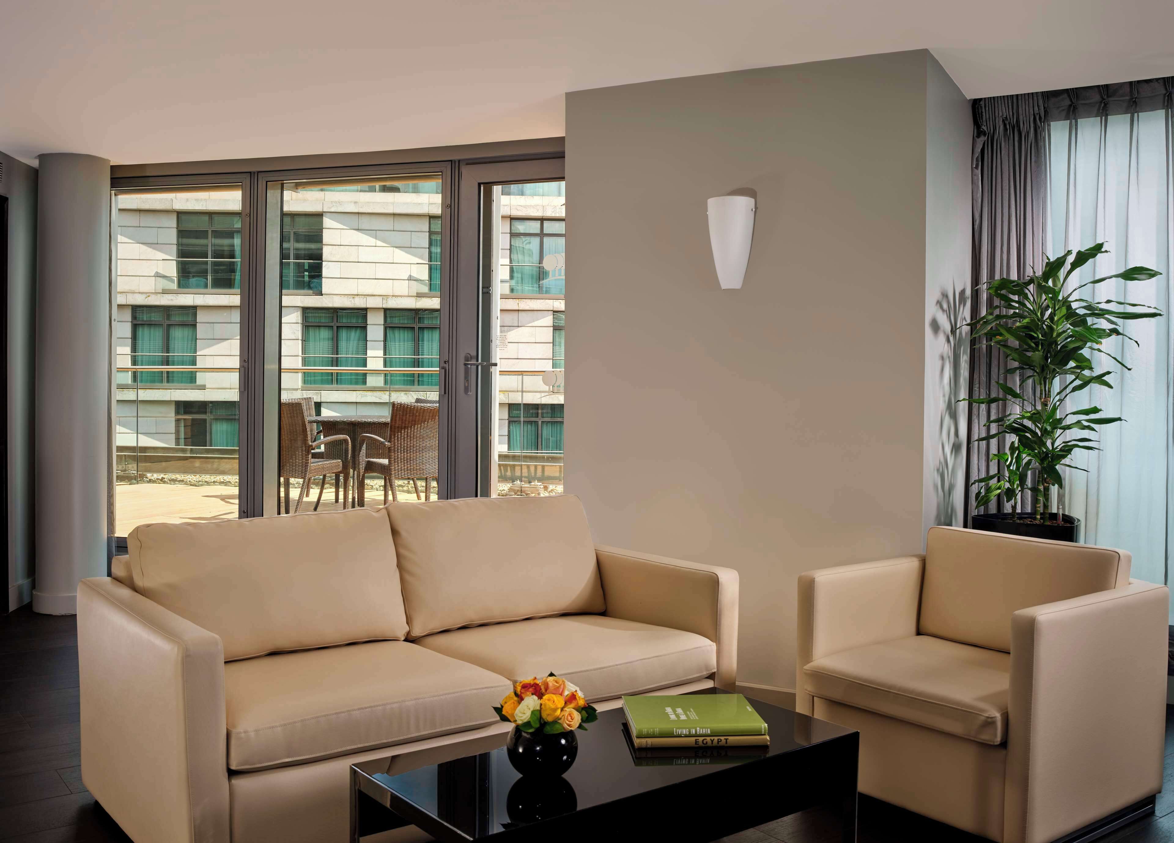 A modern living room with a sofa, armchair, and a coffee table with a book and flowers.