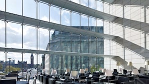 Un hall d’hôtel moderne, doté de grandes fenêtres, de sièges en cuir noir et offrant une vue sur le paysage urbain.