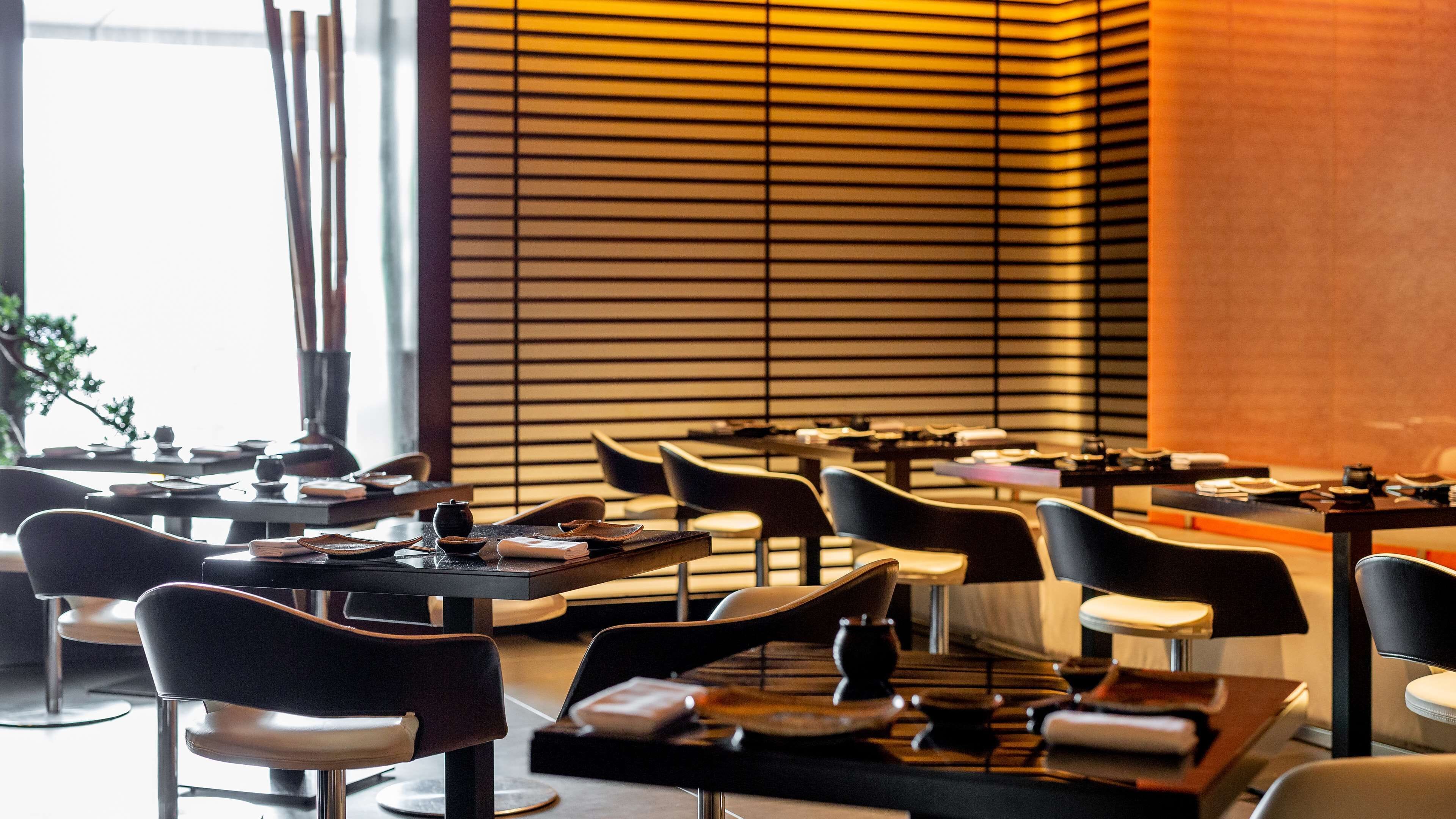A modern restaurant interior with tables, chairs, and a slatted wall design.