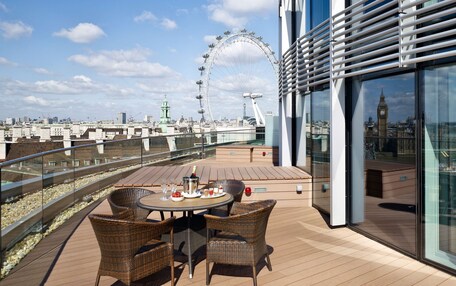 A rooftop terrace with a table set for dining, wicker chairs, and a view of the London Eye and Big Ben.