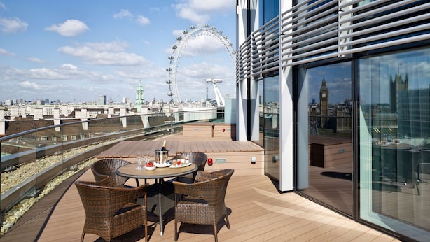 Une terrasse sur le toit, avec une table dressée pour le dîner, des chaises en osier et une vue sur le London Eye et Big Ben.