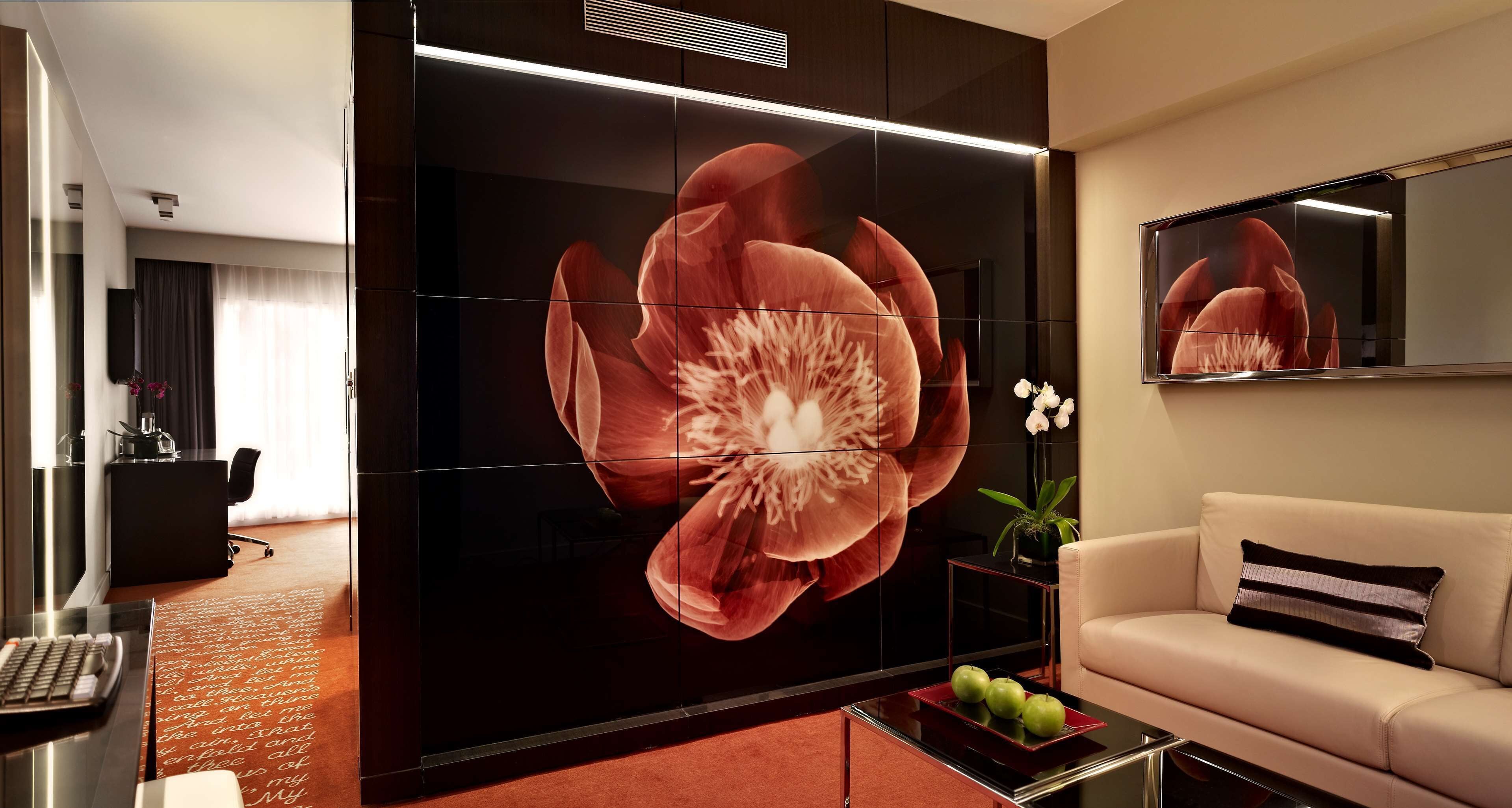 Una sala de estar moderna con un gran cuadro floral, un sofá, una mesa de centro con objetos decorativos y un escritorio con un teclado.