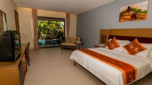 A hotel room with a bed, a TV, a desk, a chair, a small table, and a view of a pool and greenery. - The Natsepa Resort & Conference Center (Salahutu)