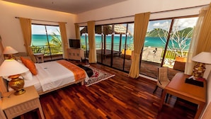 A hotel room with a large bed, a desk, a TV, and a balcony with a view of the ocean. - The Natsepa Resort & Conference Center (Salahutu)