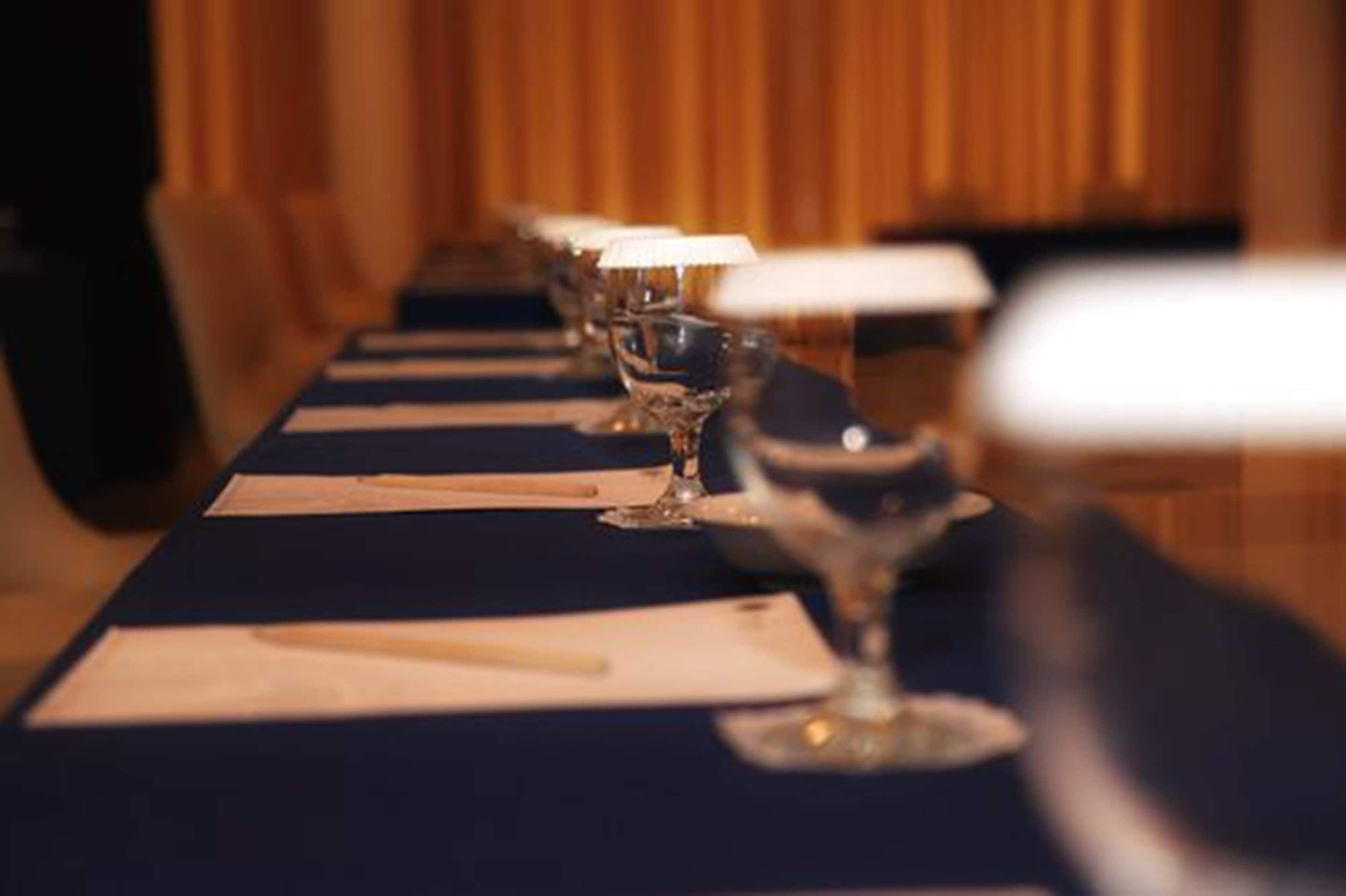 Une longue table, parée de nombreux verres à vin et de serviettes, se dressant devant un décor en bois.