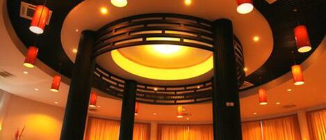 Un vestíbulo de hotel con una zona de estar circular, ventanas amplias con cortinas y luminarias modernas.