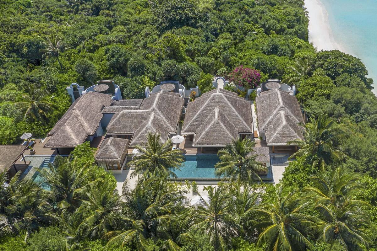 An aerial view of a resort with thatched-roof bungalows, a swimming pool, and a beach.