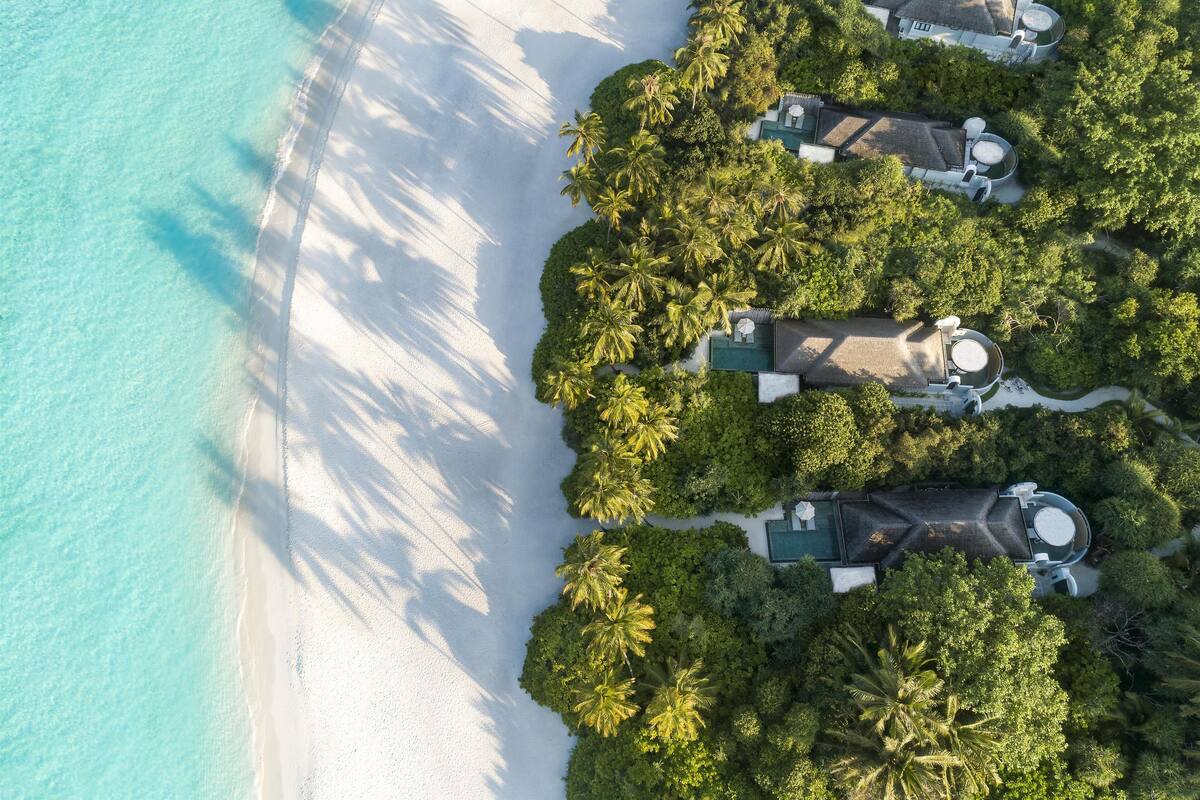 An aerial view of a resort with multiple villas, a beach, and lush greenery.