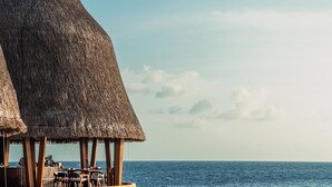 A seaside restaurant with thatched roofs and wooden deck chairs overlooking the ocean. - Anantara Kihavah Maldives Villas (Kihavah)