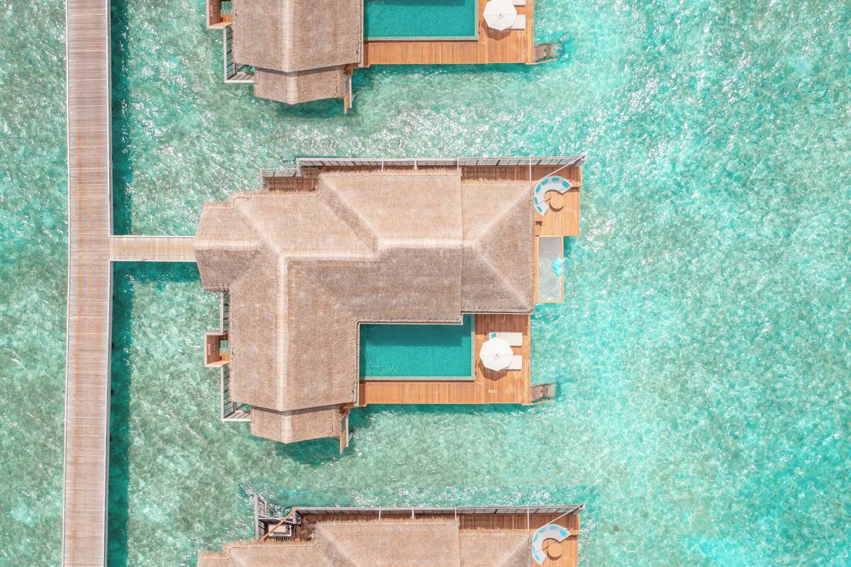 An aerial view of a resort with multiple overwater bungalows connected by a wooden walkway.