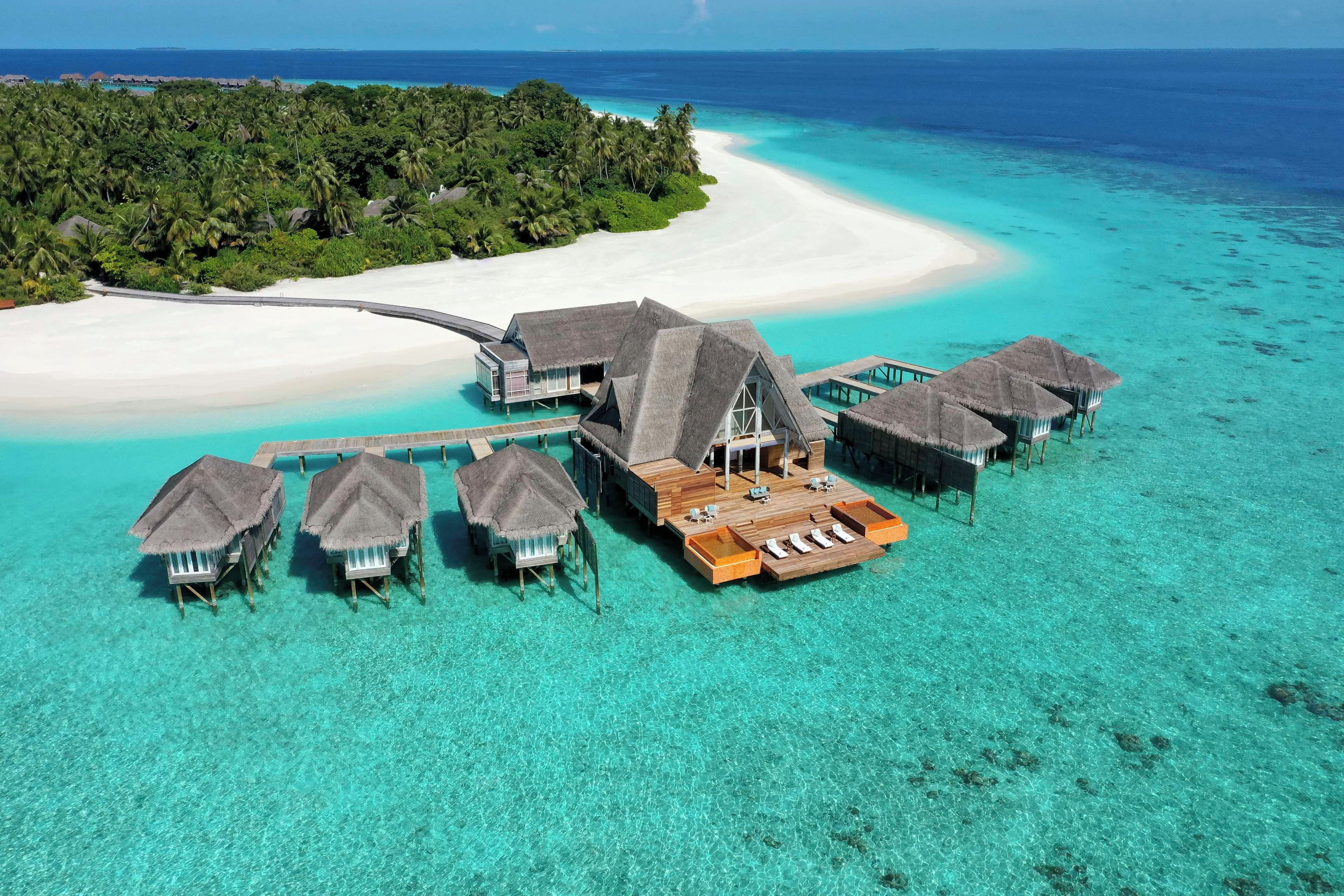 An overwater bungalows with thatched roofs and wooden walkways over clear turquoise waters.