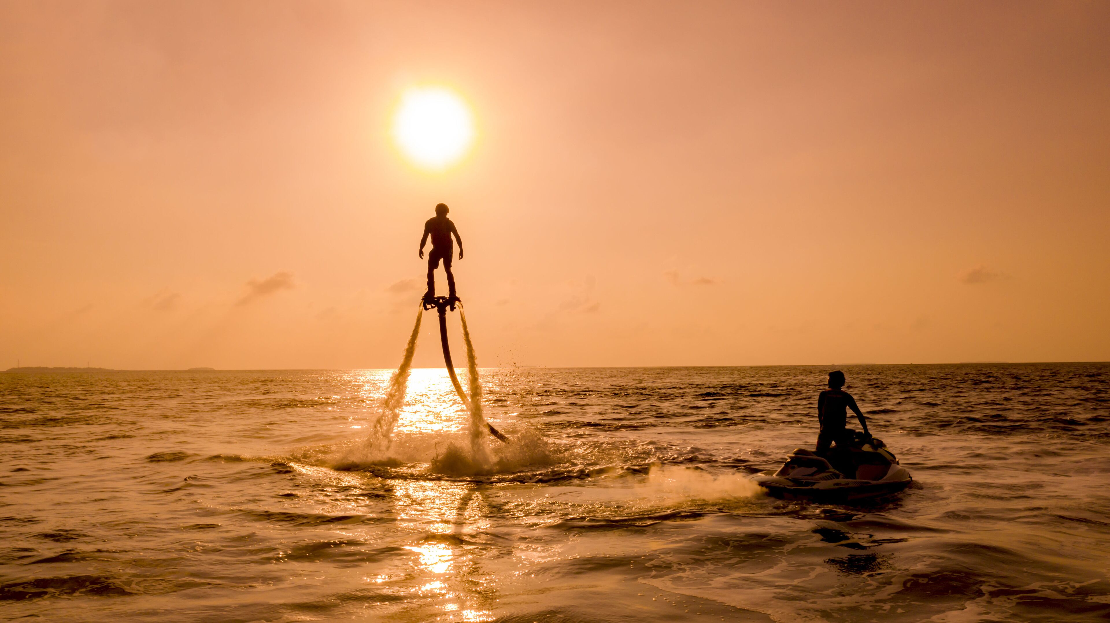 A sunset over the ocean with two people engaging in water activities.