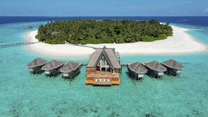 An overwater bungalows with a central wooden deck, surrounded by clear turquoise waters and a white sandy beach. - Anantara Kihavah Maldives Villas (Kihavah)