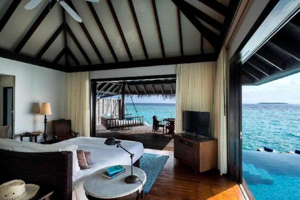 A bedroom with a bed, bedside table, lamp, and a TV. There is a balcony with a view of the sea.