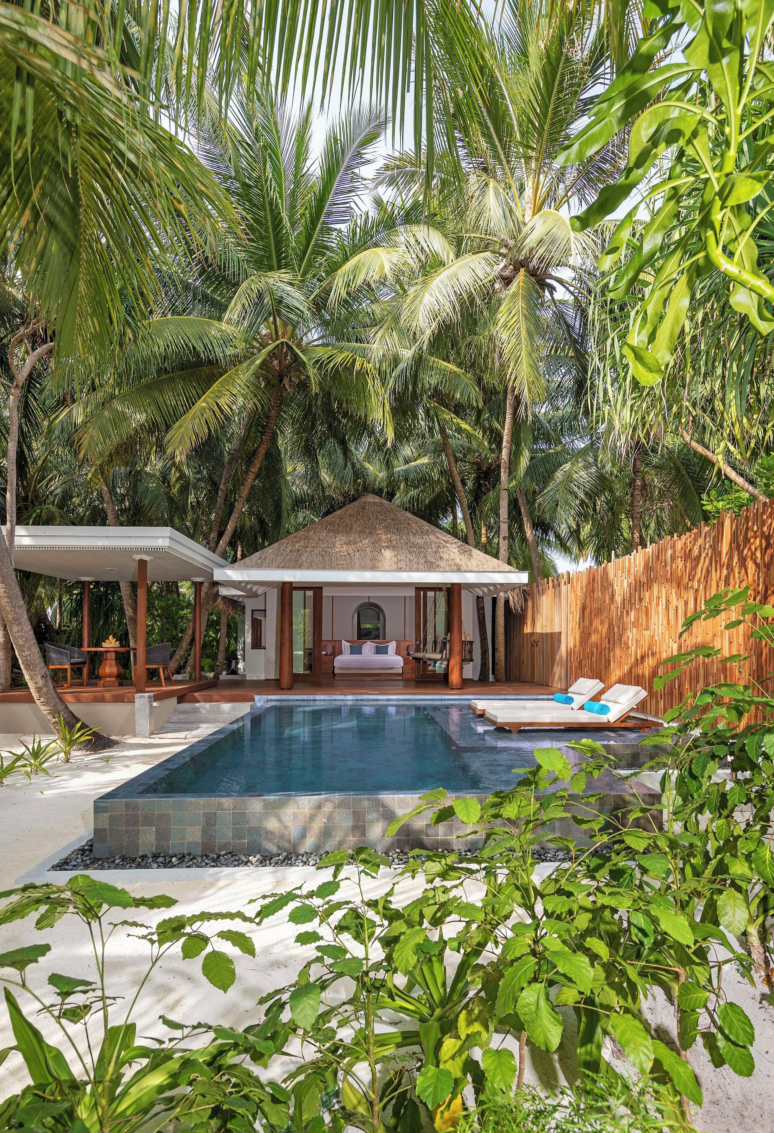A poolside area with a house, a wooden fence, and palm trees.