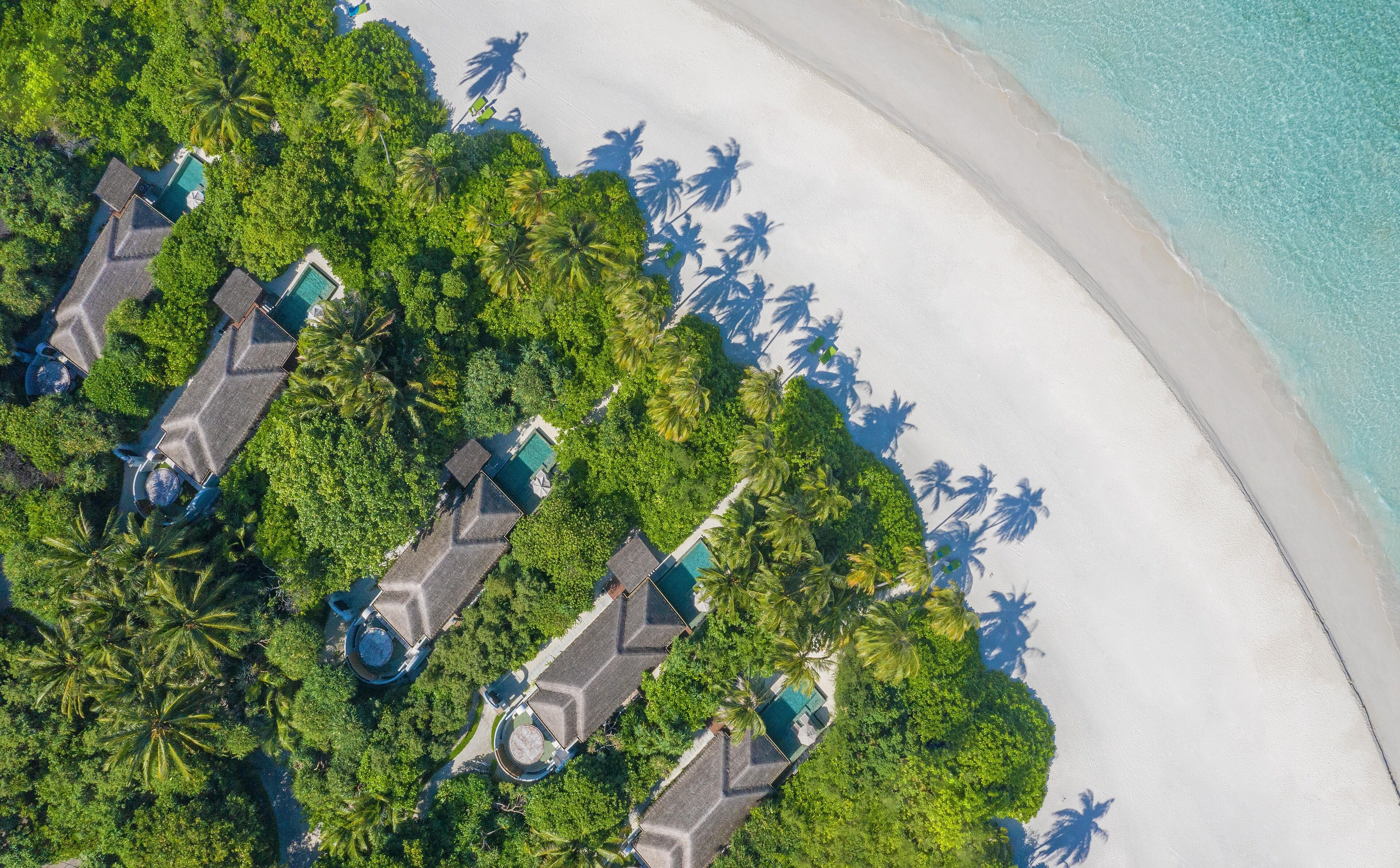 Vista aérea de un resort con múltiples alojamientos tipo bungaló, una playa de arena y abundante vegetación.
