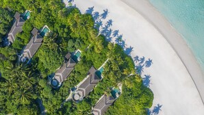 An aerial view of a resort with multiple bungalow-style accommodations, a sandy beach, and lush greenery. - Anantara Kihavah Maldives Villas (Kihavah)