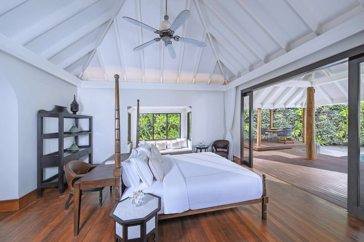 A bedroom with a bed, a desk, a chair, a bookshelf, and a view of an outdoor deck.