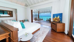 A spacious bedroom with a large bed, a wooden desk, a TV, and a view of the ocean. - Anantara Kihavah Maldives Villas (Kihavah)