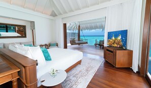 A spacious bedroom with a large bed, a wooden desk, a TV, and a view of the ocean. - Anantara Kihavah Maldives Villas (Kihavah)