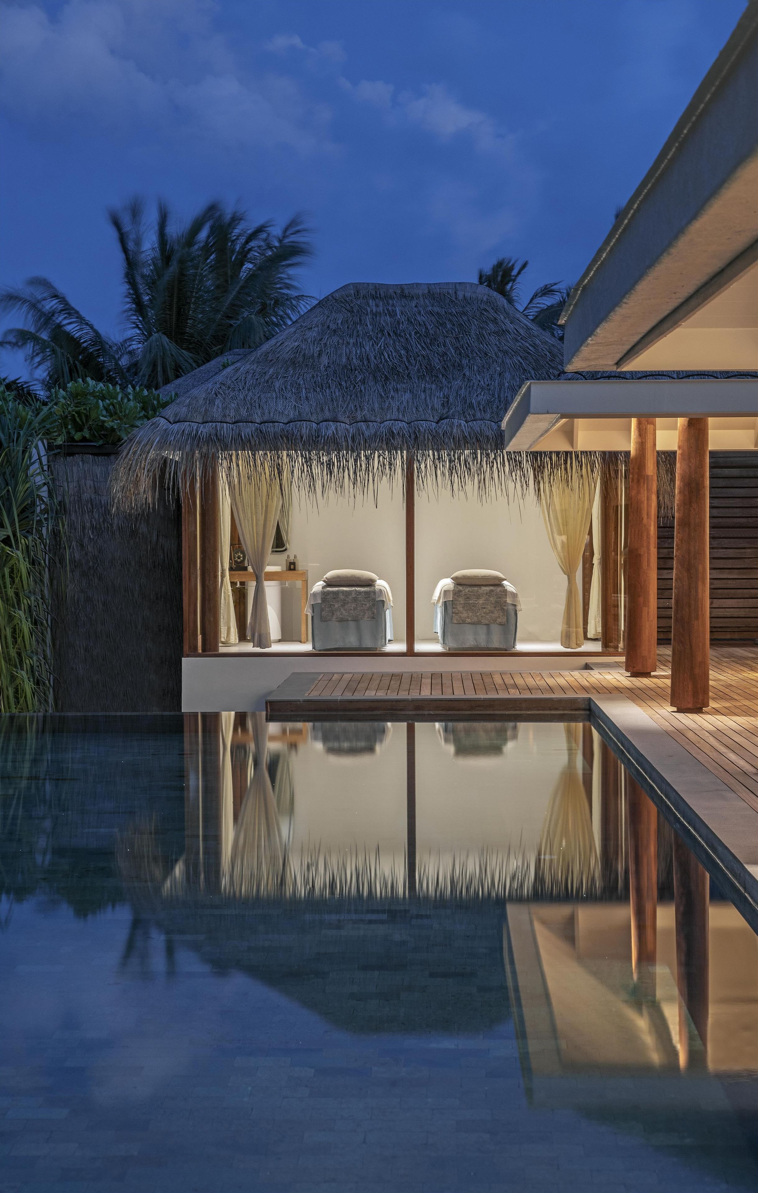 Una piscina infinita tranquila con una estructura de techo de paja, dos sillones mullidos y una terraza de madera.