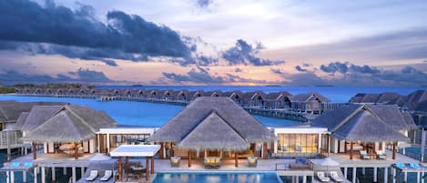 Overwater bungalows with infinity pools, a clear view of the ocean, and a sunset sky.