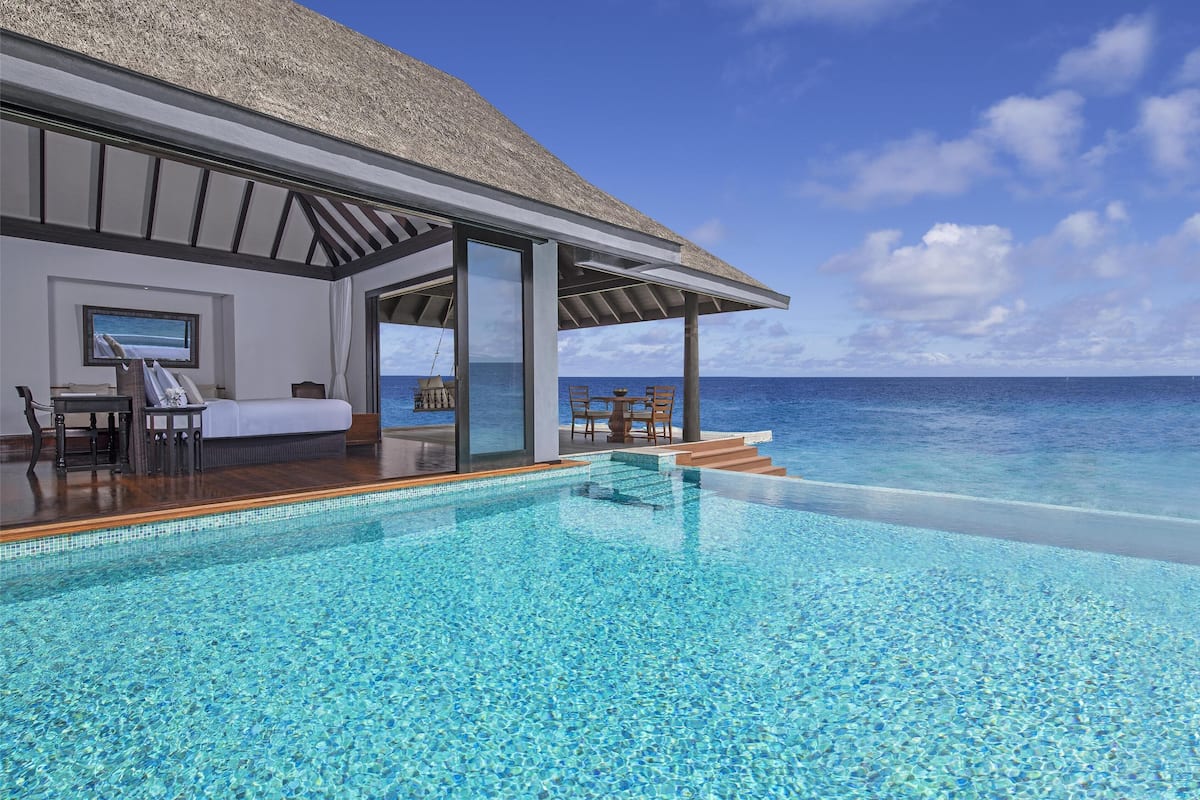 A modern infinity pool with clear blue water, a thatched roof structure, and a view of the ocean.
