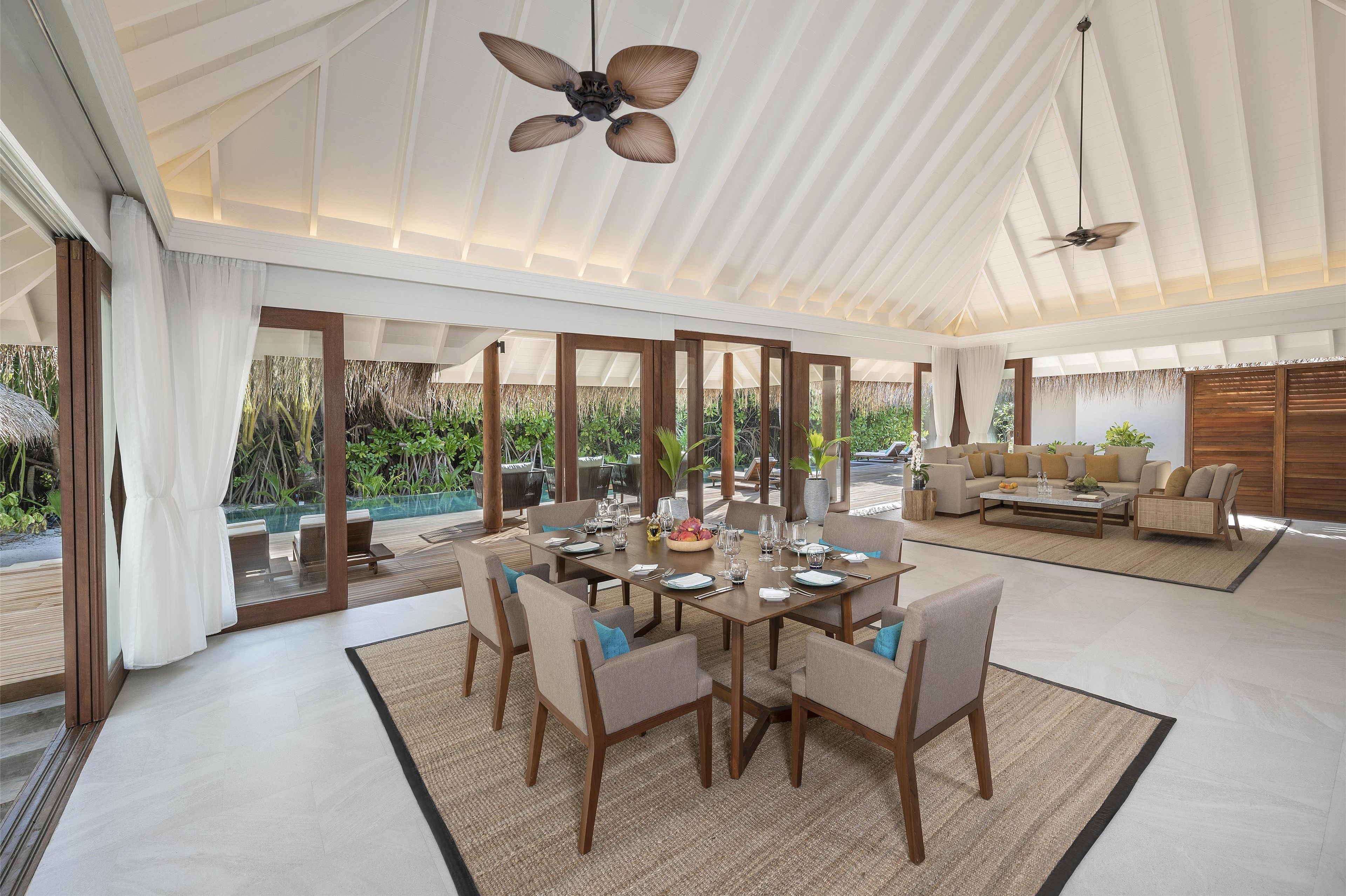 A spacious dining area with a high ceiling, large windows, and a view of the surrounding greenery.
