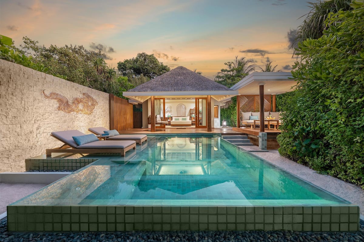 A modern pool area with lounge chairs, a hot tub, and a covered seating area.