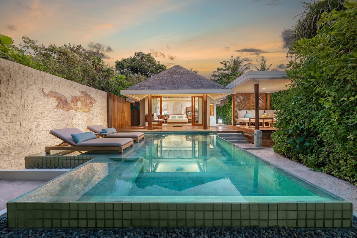 Un área de piscina moderna con sillones de descanso, una bañera de hidromasaje y una zona de estar techada.