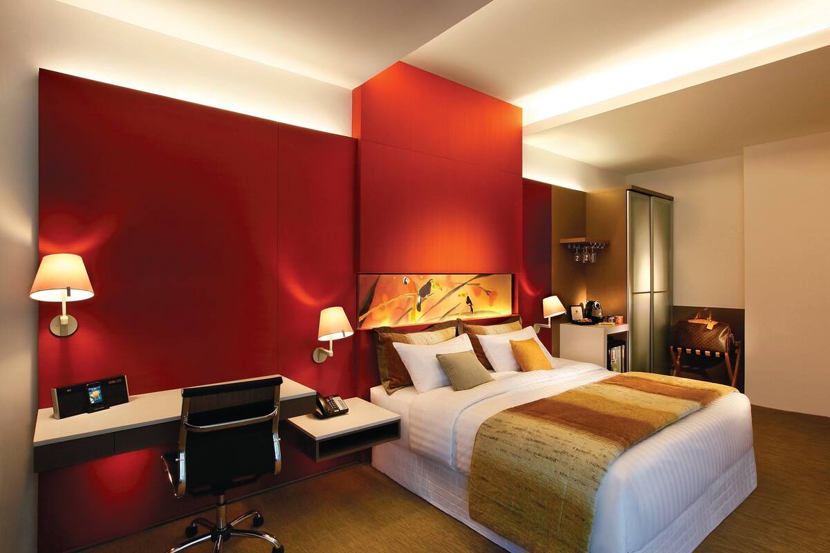 Una habitación de hotel moderna con una cama grande, un escritorio con una silla, una lámpara de escritorio y un televisor montado en la pared.