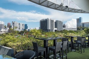 An outdoor seating area with tables and chairs, surrounded by greenery and overlooking a cityscape with modern buildings. - D'Hotel Singapore managed by The Ascott Limited (Singapore)