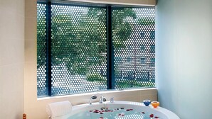 A modern bathroom with a freestanding bathtub, a small round table with a bottle and glasses, and a window with a view of greenery. - D'Hotel Singapore managed by The Ascott Limited (Singapore)